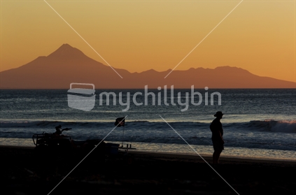 A lone fisherman silhouetted at dusk under Mt Taranaki / Egmont at Mokau beach
