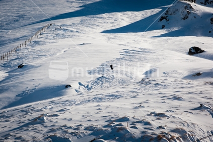 A snowboarder waving and riding down a snow covered Manganui skifield, Mt Taranaki / Egmont.