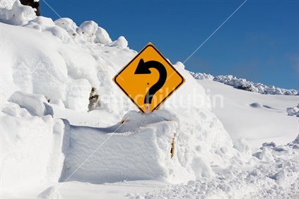 A sharp corner road sign showing through deep snow on the side of Bruce Rd, Whakapapa, Mt Ruapehu