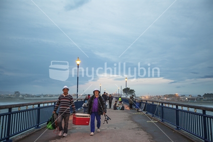 Island couple and Asian people behind, walking along New Brighton pier to fish. (raised ISO)