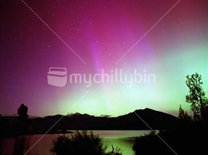 Aurora Australis, southern lights. Pink rays and the green arch reflect colours on Lake Brunner, South Island, NZ