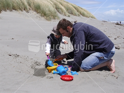 Father and son playing in the sand building sandcastles at the beach