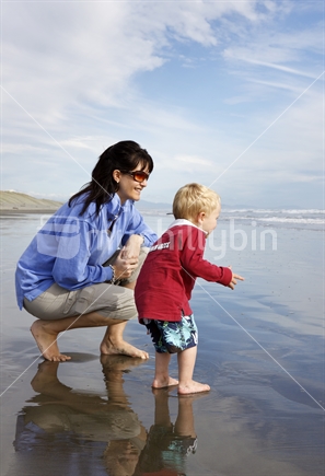 Mother with excited son paddling at the beach. 