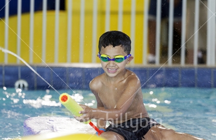 Young boy playing a game with the water pump at an indoor swimming pool.  (Raised ISO)