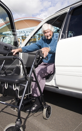 Elderly woman getting out of the car using her mobility walker for support.