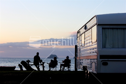 Campers enjoying the sunset with a picnic beside a caravan.