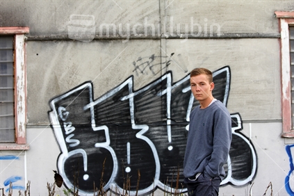 Teenage boy standing by  derelict building with graffiti in background