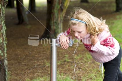 Young Girl drinking from a water fountain in the park