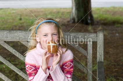 Young girl sitting on a park bench holding a Hot Cross Bun
