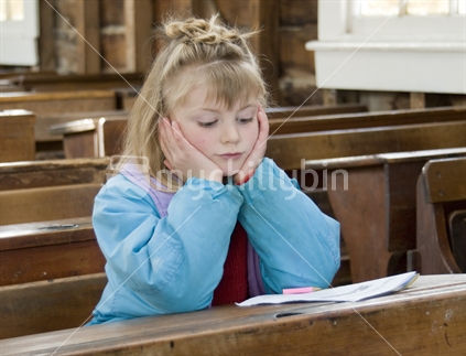 Young girl sitting with her head in her hands at a desk  in an old fashioned School room