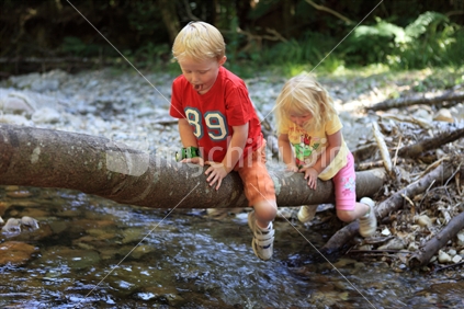 Young boy and girl crossing river using tree trunk