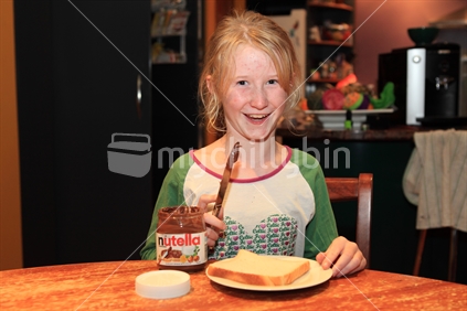 Cheeky young girl eating a Nutella sandwich for breakfast