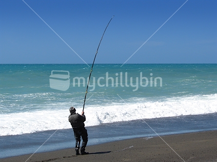 A fisherman surf casting, New Zealand