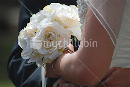 A brides embraced by her hubby to be, holding a beautiful bouquet
