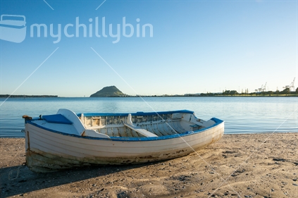 Blue and white clinker dinghy on beach with Mount Maunganui on horizon beyond.