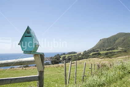 Turquoise letterbox perched on a fence post with one of the worlds best views, from Highway 35 near the East Cape.