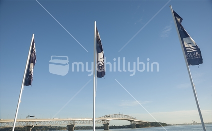 Auckland Harbour Bridge through three Club Marine Insurance flags, stretching to the horizon from  Westhaven  after sunrise in March 2014.