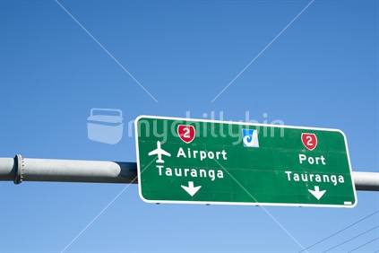 Airport and Port Tauranga highway direction sign over Hewletts Road or state Highway 2, Tauranga against a blue sky.