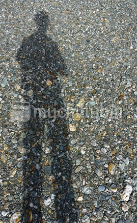 Long shadow, male figure projected onto stony river bed.