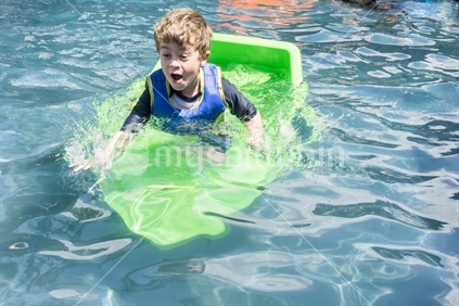 Small boy plays at sinking boat. Symbolic of water and boating risks. Toy boat in swimming pool goes down while boy's face shows surprise at the danger of situation. December 26, 2015.