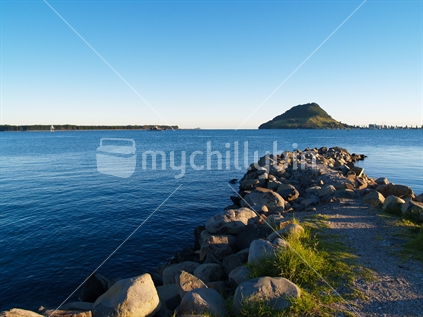 Mt Maunganui from Tauranga side of harbour, early morning on a clear day, with rocky foreground. North Island, New Zealand.