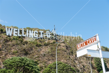 Windy Wellington sign on hillside at Miramar in white corrugated iron mounted on side of hill to look like itis blowing away  with Weta Cave tourism sign below.