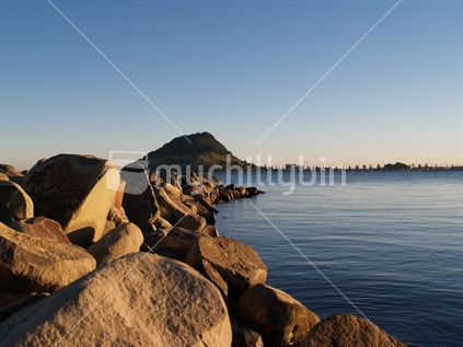 Mt Maunganui from Tauranga side of harbour, early morning on a clear day, with large close up rocky foreground. North Island, New Zealand.