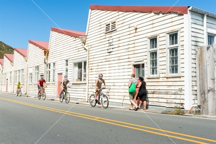 People enjoying summer day out walking and cycling past old white naval weathered warehouse buildings Shelly Beach Road, Miramar, Wellington New Zealand
