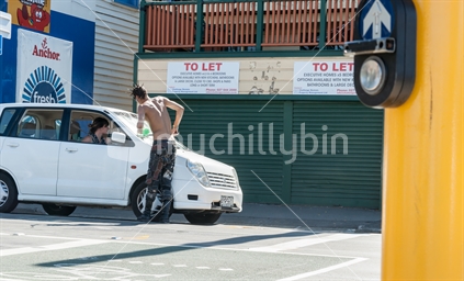 Street scene of bare backed with spiky hair Wellington street car window washer Willis Street  cleans windscreen of car stopped at intersection lights February 2016