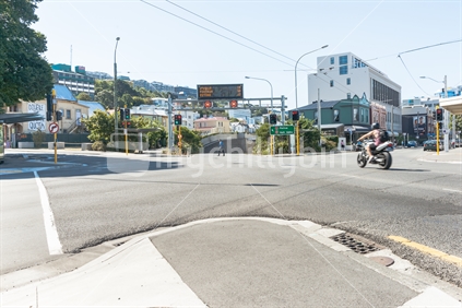 Wellington Intercity  By-Pass intersection with Willis Street with overhead  illuminated travel time advisory sign as motorcycle blurred in motion passes and man in blue shirt walks across street. February 2016.