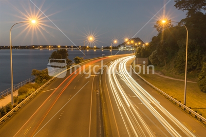 Tauranga Takitimu Expressway in dark of night with lights of vehicles streaming highlighting movement of cars passing along road dark sky and above
