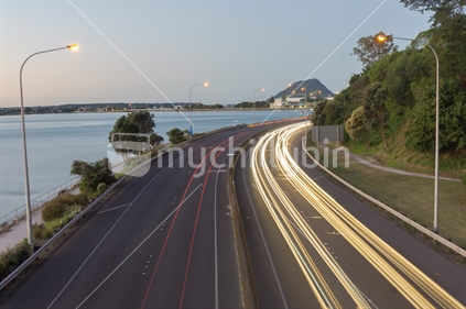 Highway red and yellow light streams along Takitimu Drive at dusk looking north with Mount Maunganui on horizon.