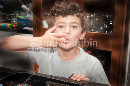 Young boy licks finger in kitchen