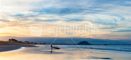 Sillhouette of lone man dragging paddleboad in hazy evening light