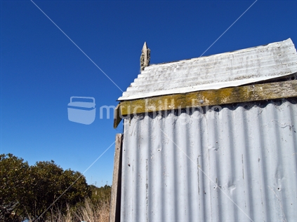 Blue sky beyond section of old corrugated iron out-house