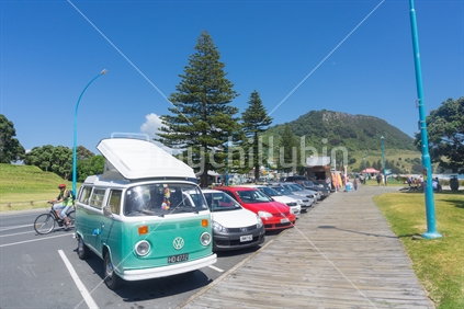 Retro lilac blue and white VW Kombi parked along Marine Parade walkway with refreshment sales kiosks leading to Mount Maunganui