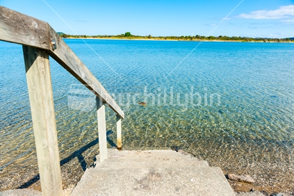Concrete steps and wooden safety handrail leading down to waters edge of scenic estuary Ngunguru as duck drifts past.