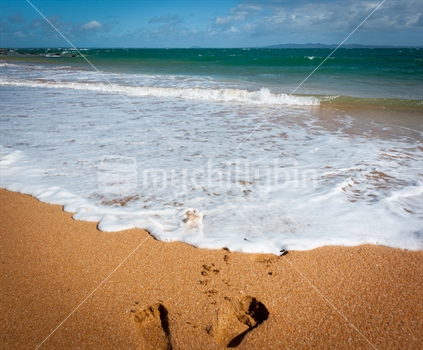 Footprints in sand about to be washed away by incoming wave and sea foam