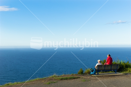 Couple sit resting near top of Mount Maunganui taking in the magnificent ocean view early evening.