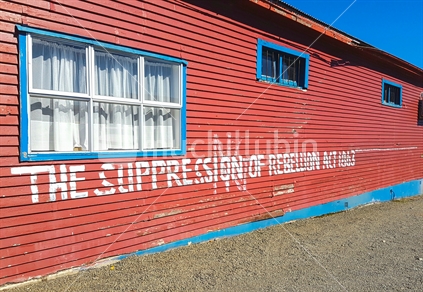 Red wall with wall art protest message on suppression of rebellion, Taneatua March 2017. 