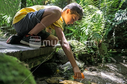 Boy in soft focus reaching into stream for drink cool clean fresh water from bush stream boardwalk in natural environment.