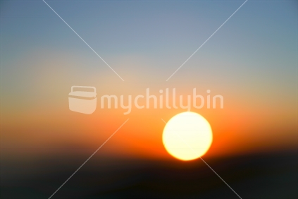 Large golden sun on horizon as sunrises defocused with abstract effecto over Auckland from top Mount Eden