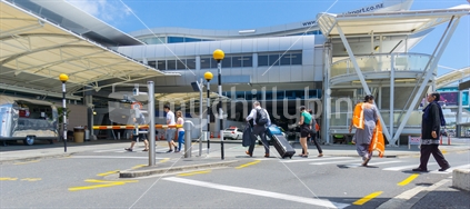 AUCKLAND, NEW ZEALAND - NOVEMBER 23, 2017 People including young couple pulling suit cases crossing road towards entranance to international airport terminal.