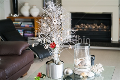 Simple summer New Zealand theme Christmas small white tree on glass table with seaside vase decoration and bright red pohutukawa flower in lounge.