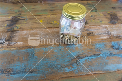 Savings jar with New Zealand currency coins and bank note  on wooden table closeup.