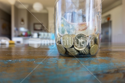 Two dollar coins Savings jar with New Zealand currency coins and bank note  on wooden table closeup.