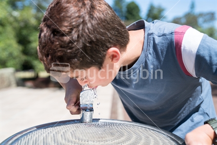 Boy at water fountain enjoying a cool drink of fresh water on a summer day.