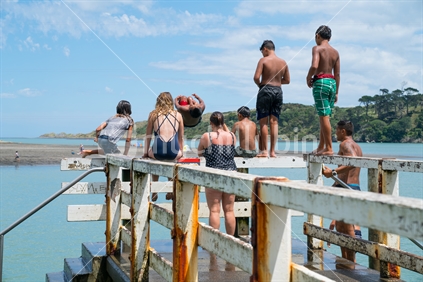 RAGLAN NEW ZEALAND - JANUARY 14, 2018; Summer fun in Raglan mostly local Maori boys jumping from the small wharf in small New Zealand town on North Island's West Coast.
