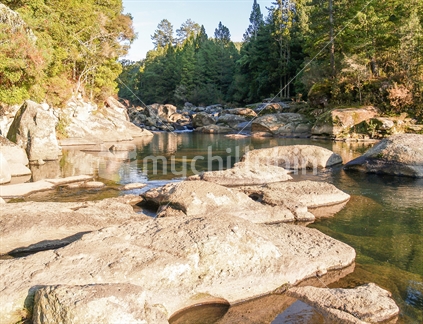 Light and shade along scenic rocky river through  tree lined gorge leading to McLaren Falls Tauranga, New Zealand