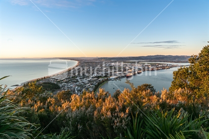 Glow of sunrise over sea and across town with ocens and harbor below from slopes of Mount Maunganui